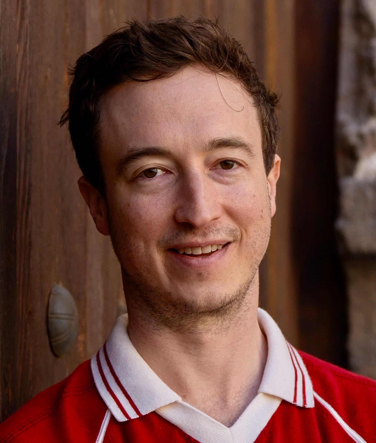Liam Lindner headshot Liam Lindner smiling in a wood doorway.